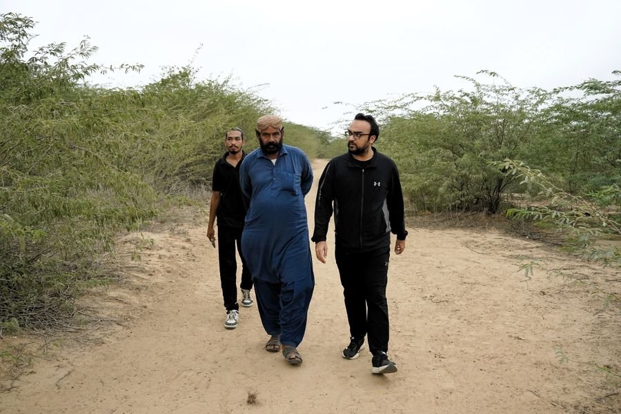 Taha Rauf walking with a community elder on a farm track during the field visit in rural Sindh